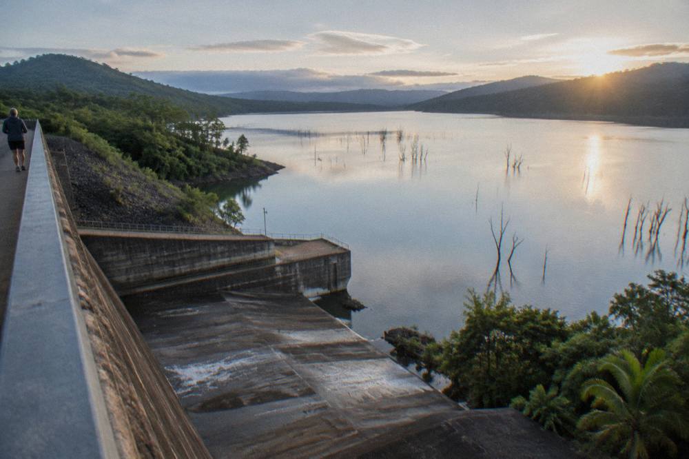 A calm stocked freshwater dam surrounded by green hills at first light