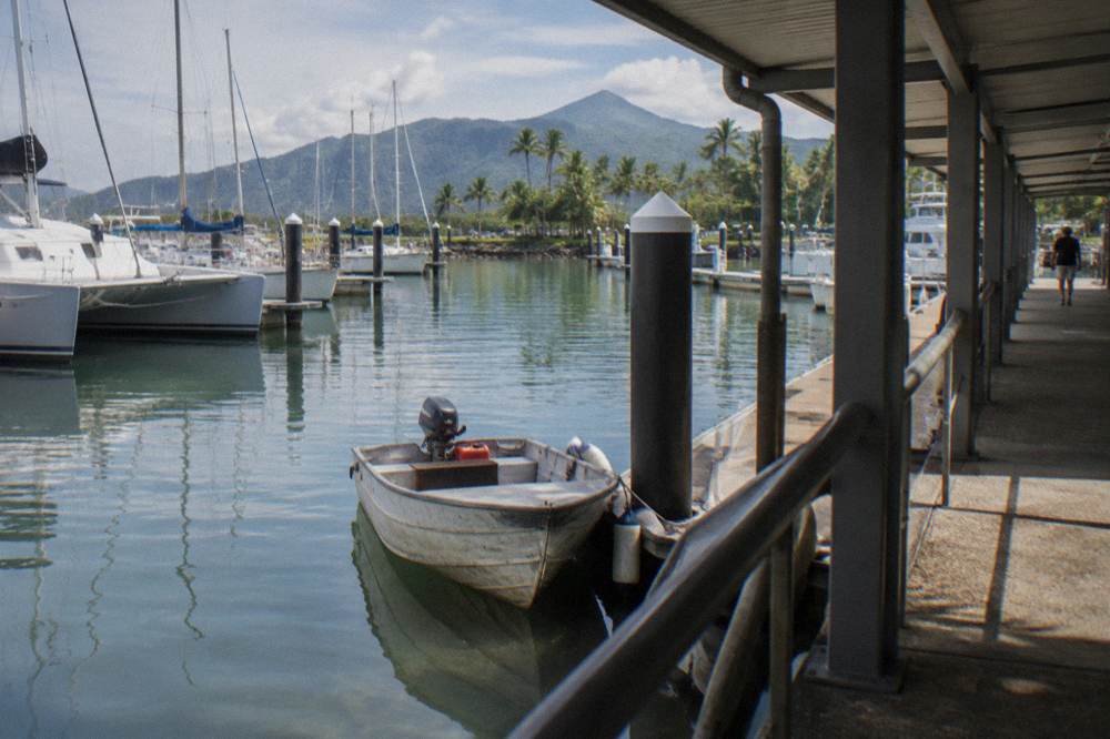 A small shaded tinny boat moored beside a marina pontoon in a tropical inlet