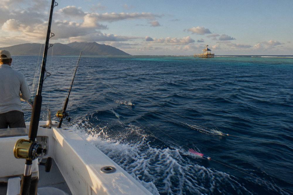 A game fishing boat trolling along the outer edge of a reef line in open blue water