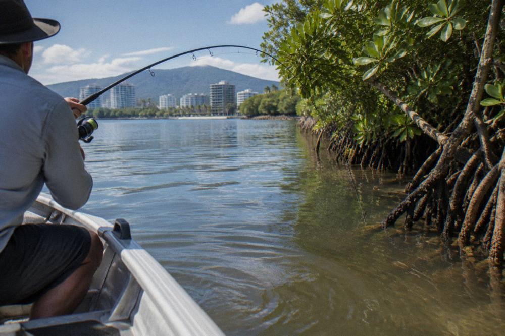 Fishing rod bent over the side of a small boat in a mangrove lined tropical inlet