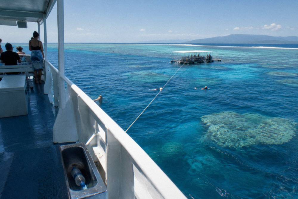 Reef boat anchored over clear blue tropical water with lines trailing toward bommies below