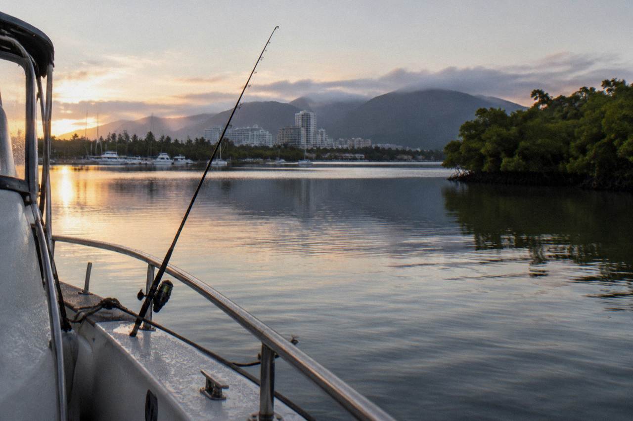 Calm tropical inlet water near mangroves at first light with a fishing rod resting against the boat rail