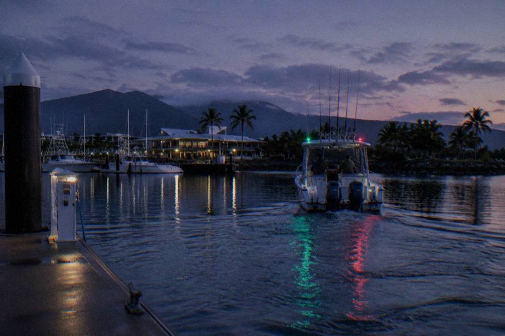 Fishing rods held upright on a small boat crossing calm water before sunrise