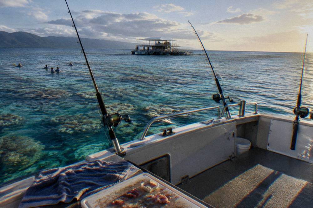 Fishing boat anchored over clear reef water with rods in holders