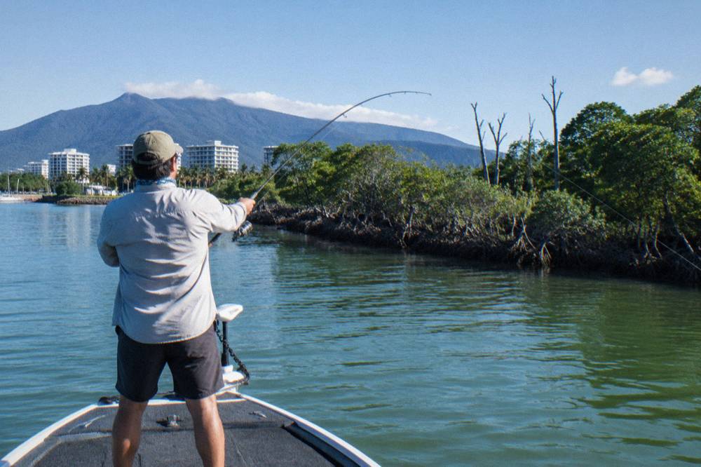 Angler casting a rod from the deck of a small boat in a mangrove estuary