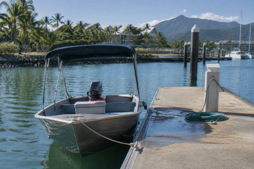 Small shaded aluminium boat moored beside a marina pontoon in the morning