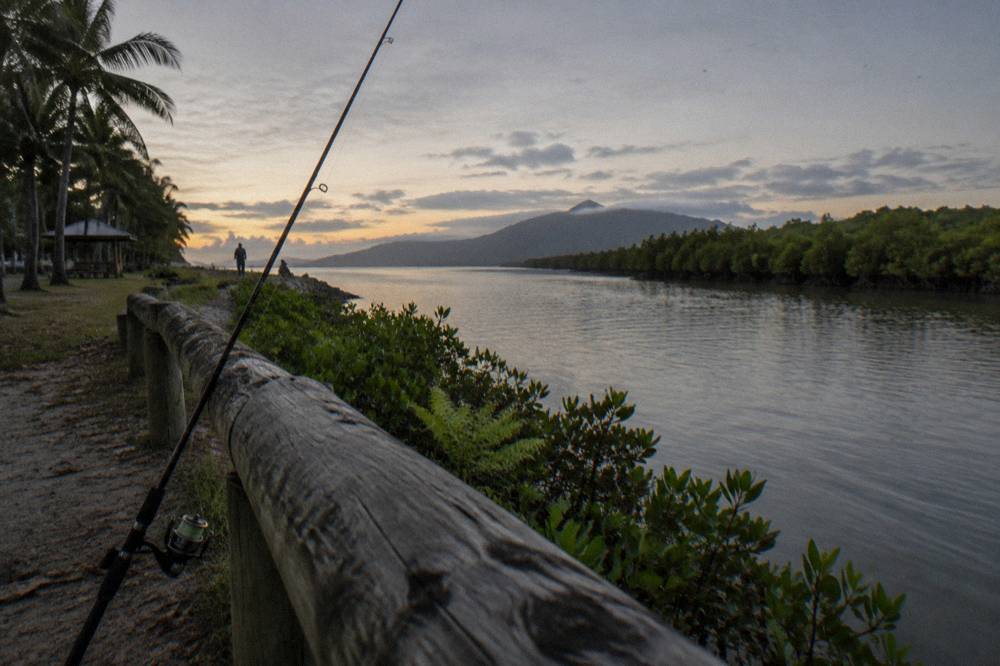 Rope fishing rod leaning against a wooden rail above calm tropical water before sunrise