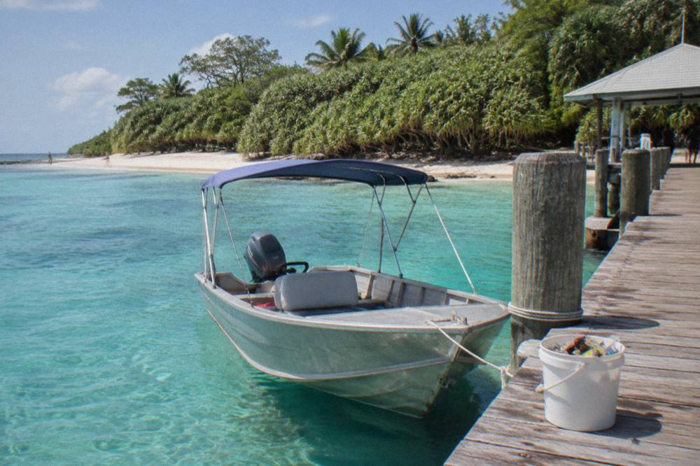 A shaded tinnie moored at a timber jetty on a mangrove-lined tropical inlet