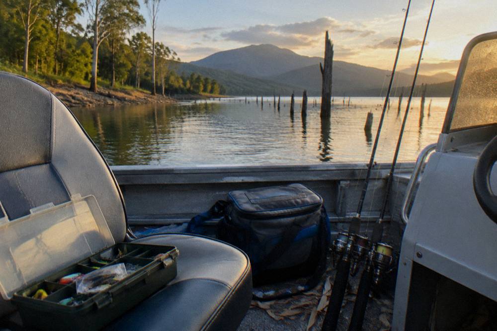 A tackle box and cooler bag open on a boat seat with rods leaning nearby