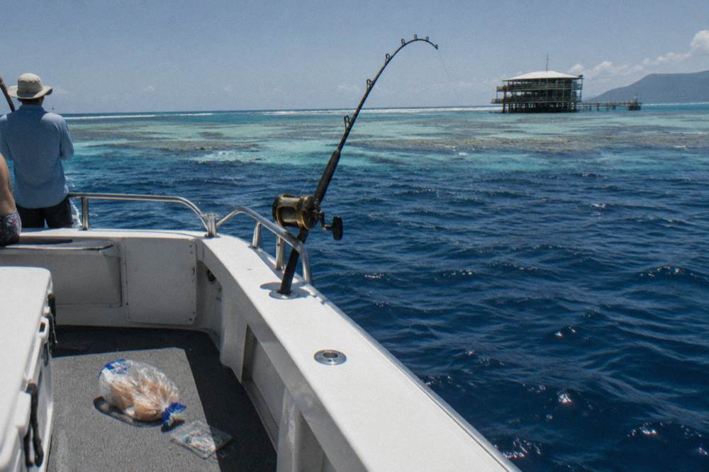 Blue open ocean beyond a reef edge with a rod bent in a holder at the stern of a boat