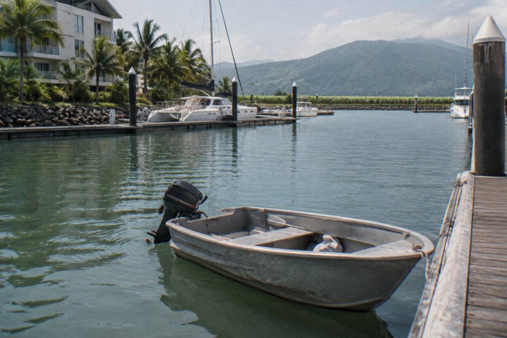 Small shaded tinny boat moored at a timber jetty beside calm green inlet water
