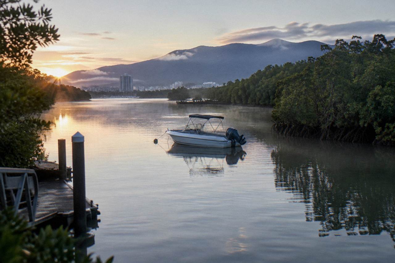 Calm water in a tropical inlet at first light with mangrove lined banks and a small boat at rest