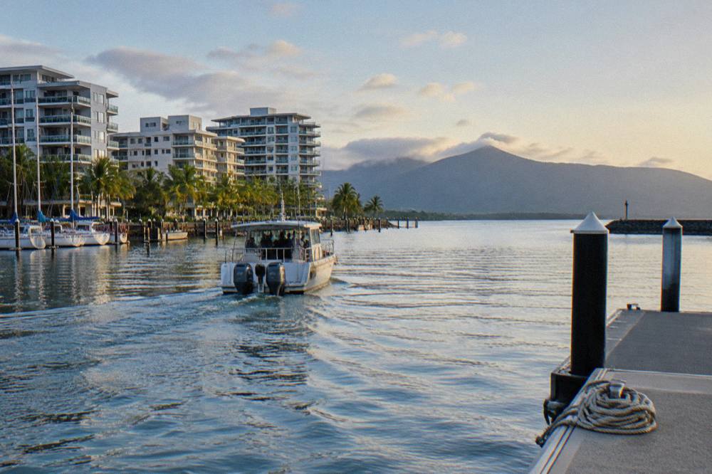 A small charter boat cruising past Cairns waterfront buildings toward open water in early morning light