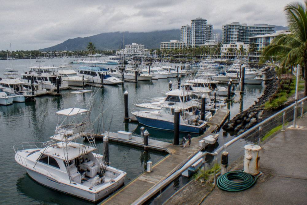 Boats moored along marina berths in Cairns with city buildings behind under a morning sky