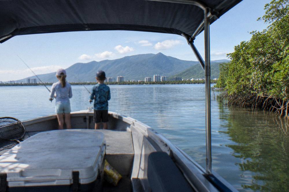 Family fishing from a small shaded boat on calm water near mangroves