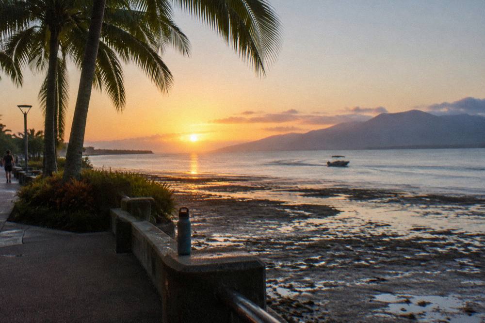 A covered small boat heading out over calm tropical water at sunrise
