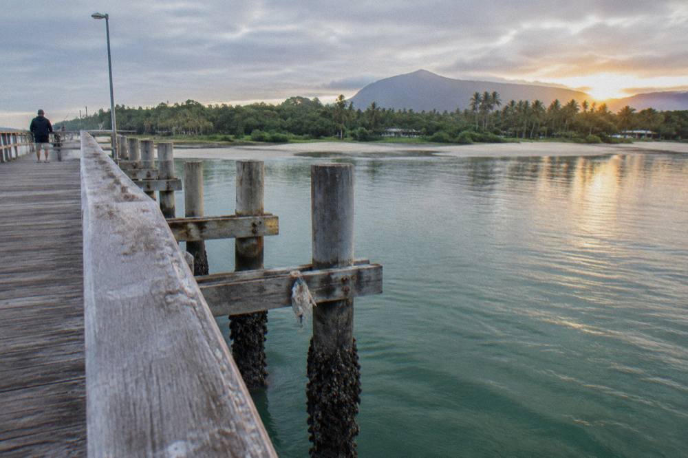 A wooden jetty stretching over calm green tropical water at first light