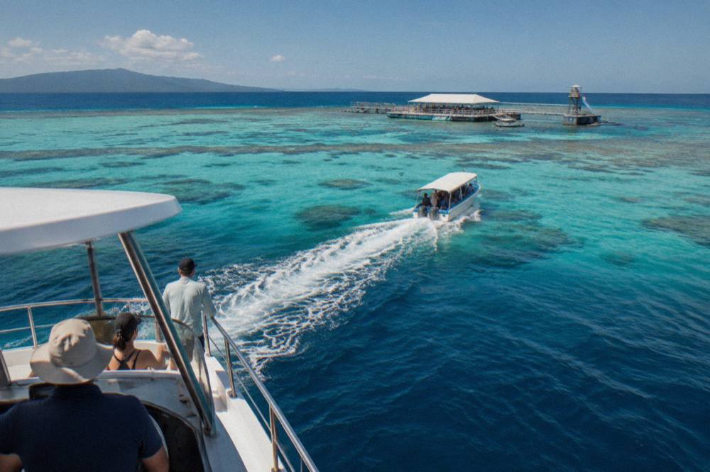 Charter boat cruising over pale blue reef shallows toward darker deeper water