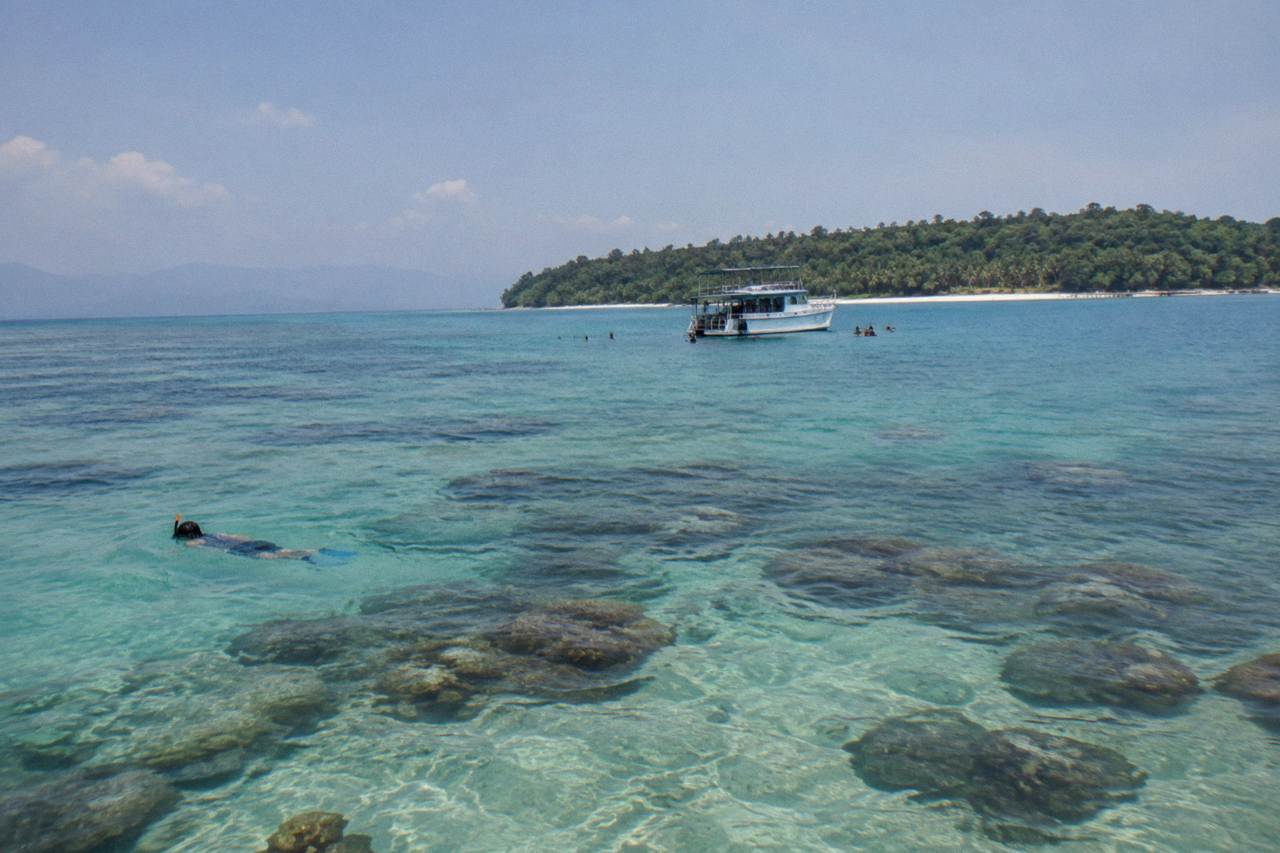 Calm turquoise reef water with coral bommies and a small charter boat anchored in the distance