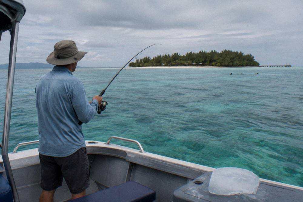 Angler reeling a fish over a reef with calm tropical water and distant reef line