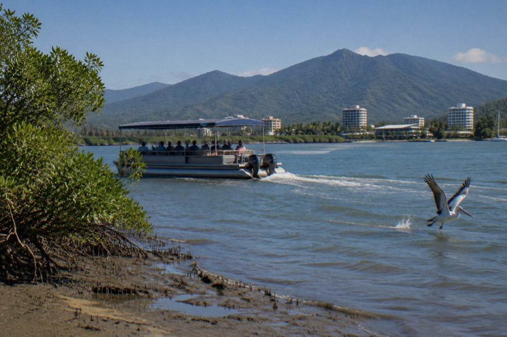 Passengers seated in a shaded pontoon boat moving through a wide tropical inlet