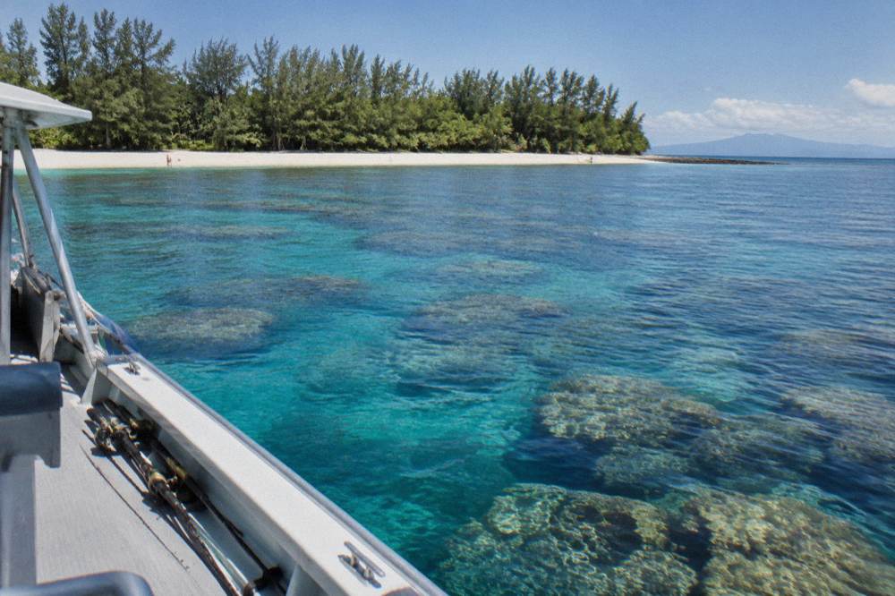 A boat underway on clear reef water with visible coral bommies below the surface