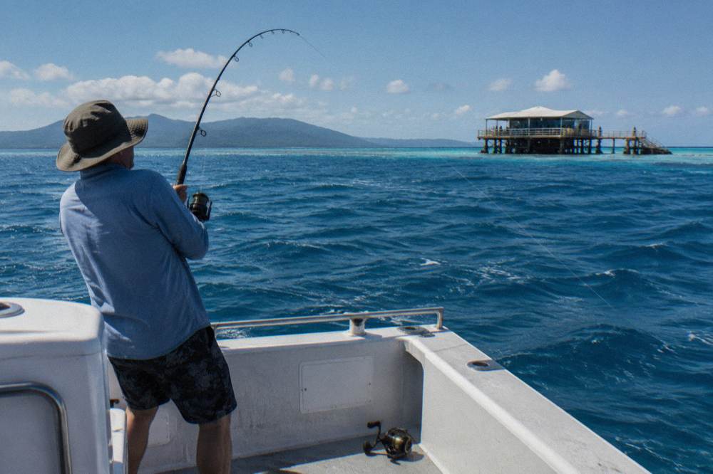 Angler reeling in a fish from the stern of a small charter boat on open water