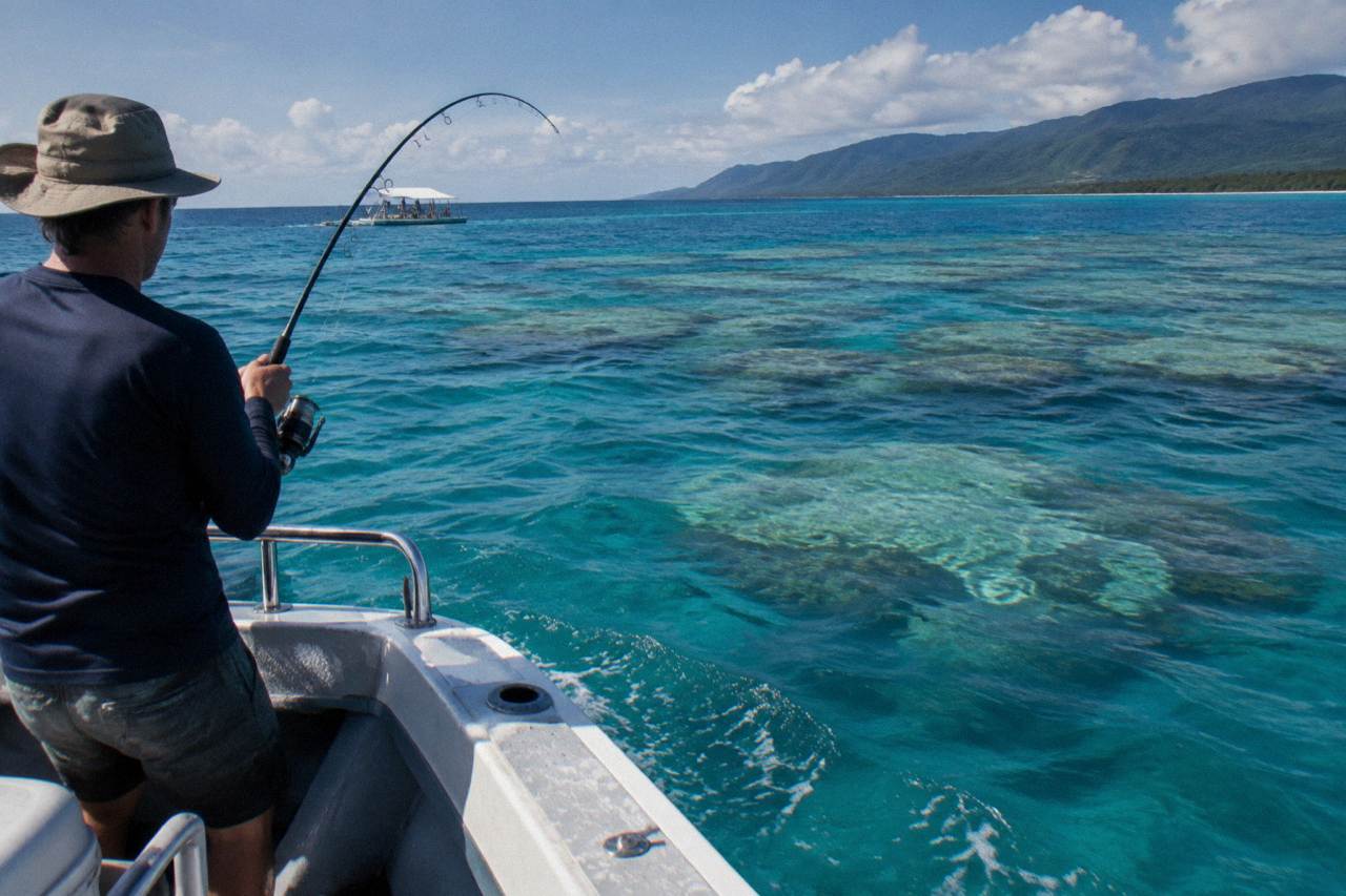 Fishing rod bent over the side of a charter boat above a coral reef in clear blue water