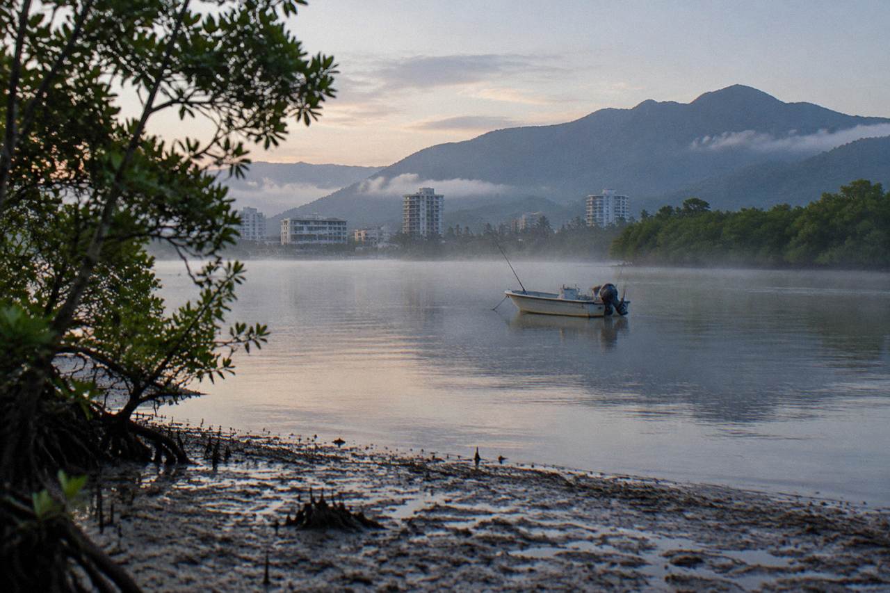 Calm mangrove-lined inlet water at dawn with a small boat holding a fishing rod