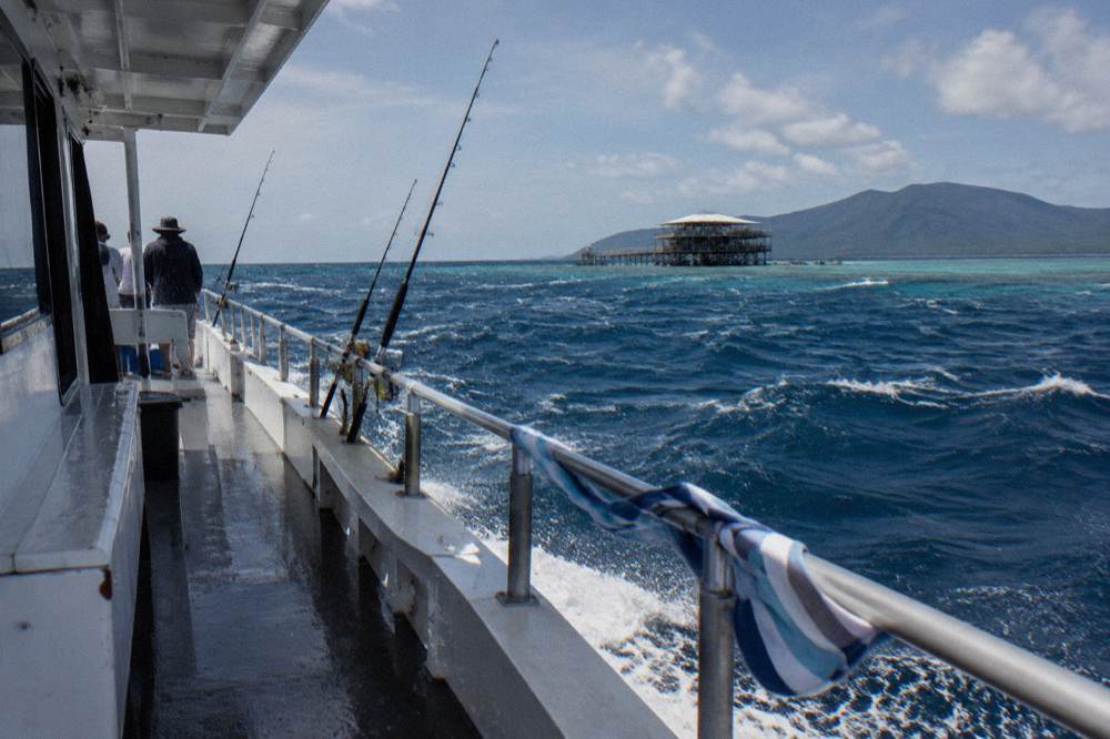 Open deck of a charter boat heading toward reef waters with rods secured forward