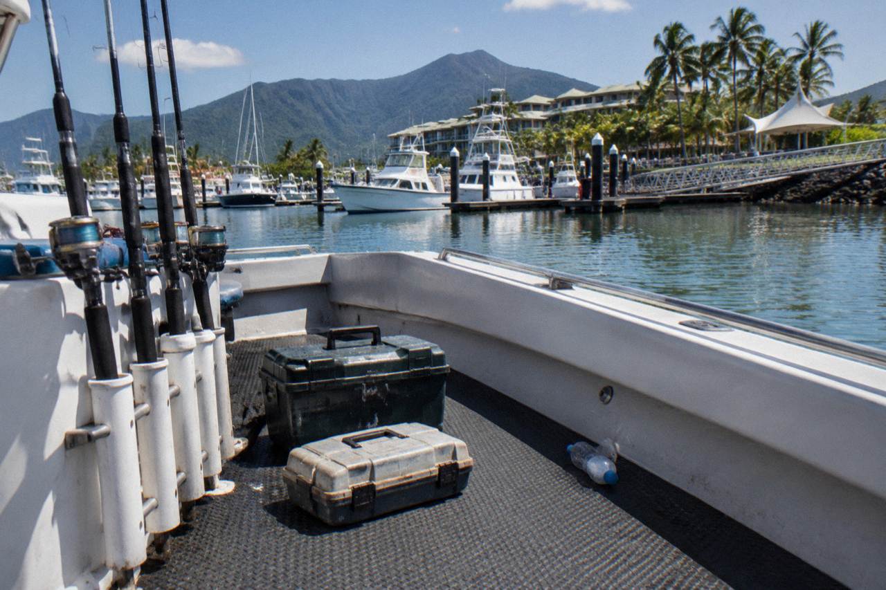 Fishing rods and tackle boxes laid out on the deck of a charter boat beside a marina